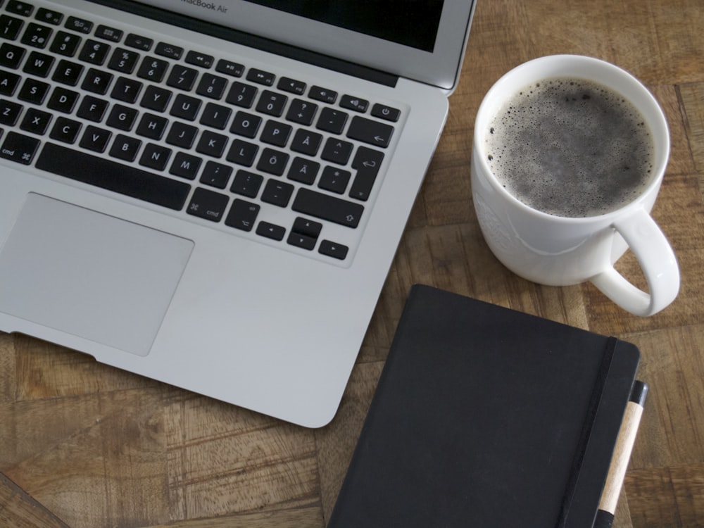 Portátil, café y cuaderno ordenados sobre un escritorio de madera